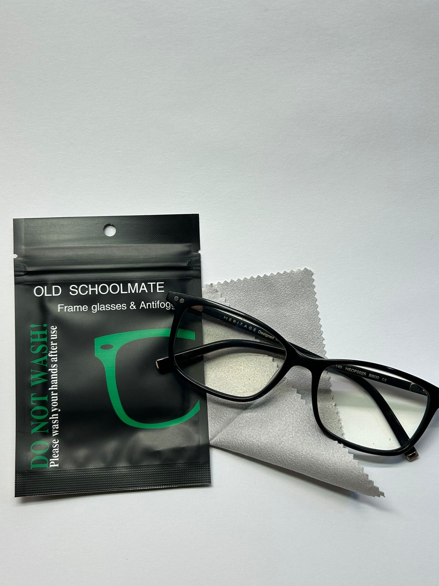 Black-framed glasses with a cleaning cloth and Old Schoolmate packaging on a white background